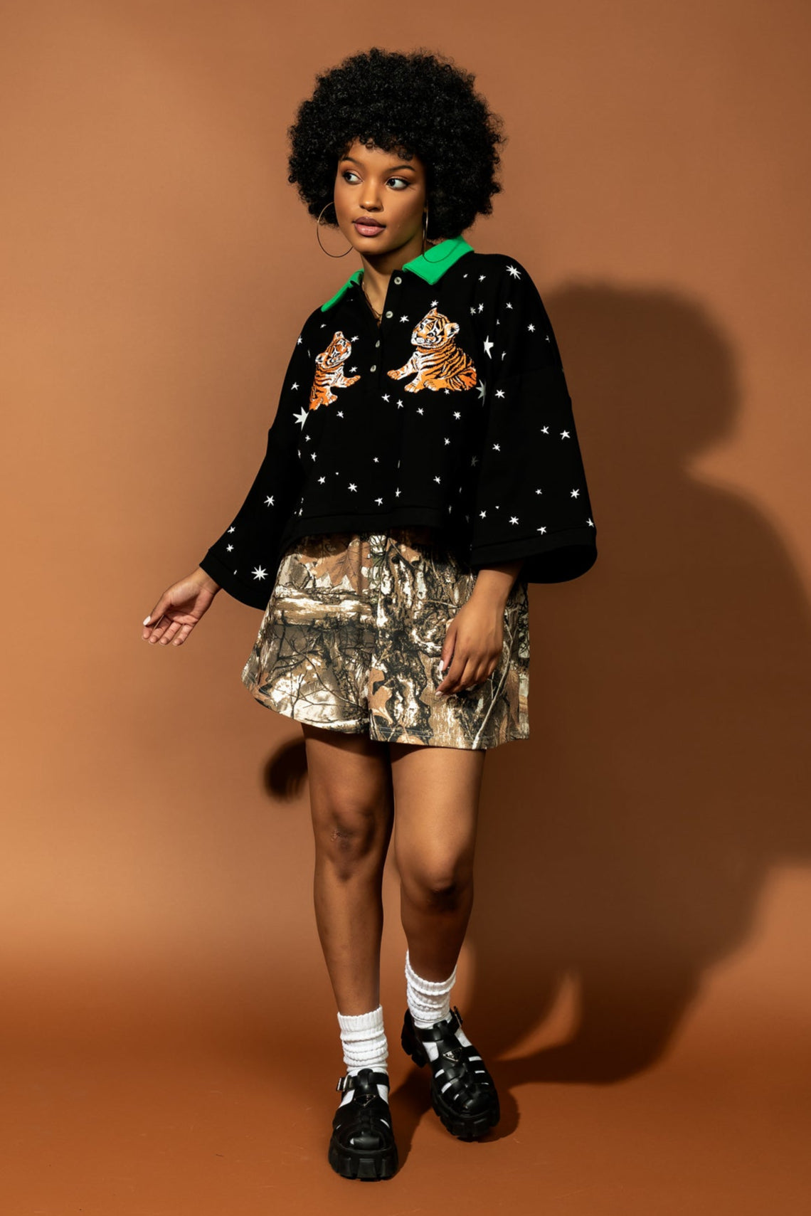 photo of girl wearing black cropped polo with green collar and white stars all over with baby tigers on the front and a baby tiger on the back words that say "made of stardust"