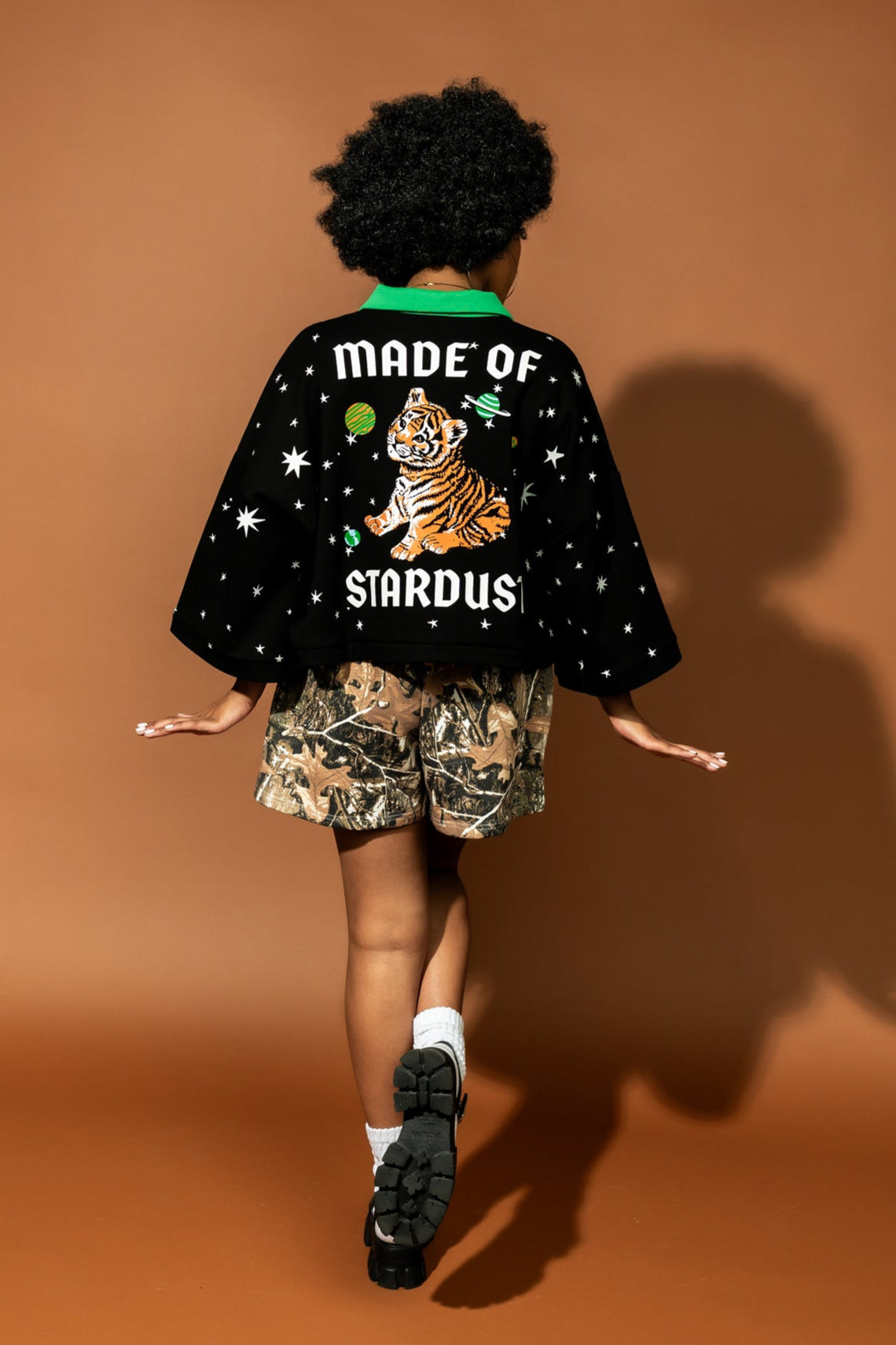 photo of girl wearing black cropped polo with green collar and white stars all over with baby tigers on the front and a baby tiger on the back words that say "made of stardust"