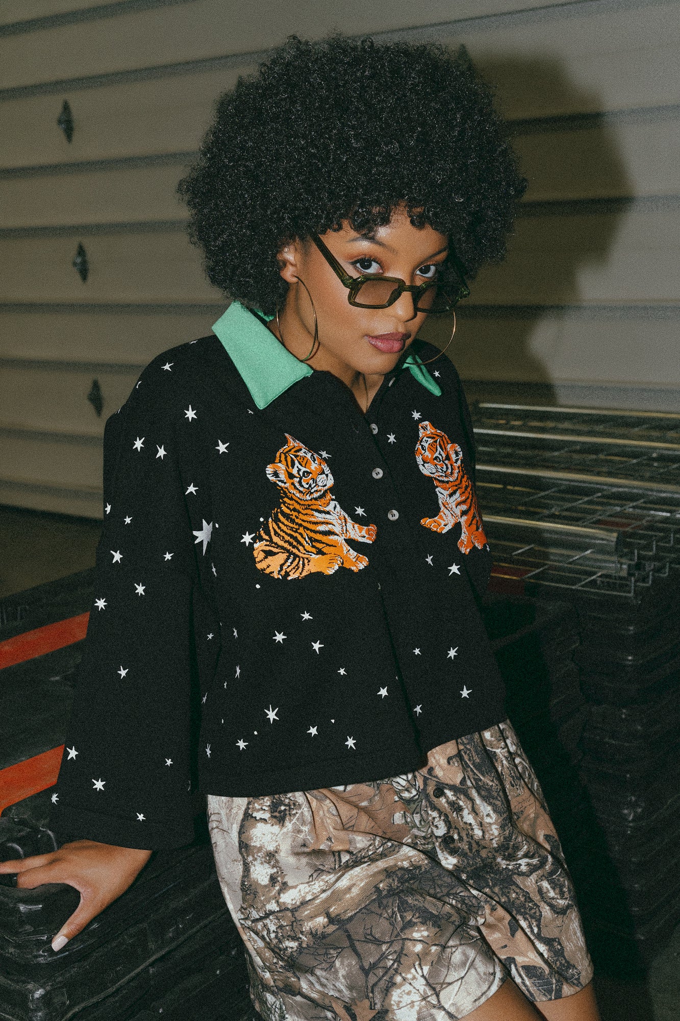 photo of girl wearing black cropped polo with green collar and white stars all over with baby tigers on the front and a baby tiger on the back words that say "made of stardust"