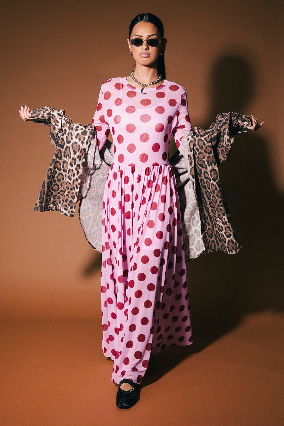 Woman in a pink polka dot dress with leopard print button up on a brown background