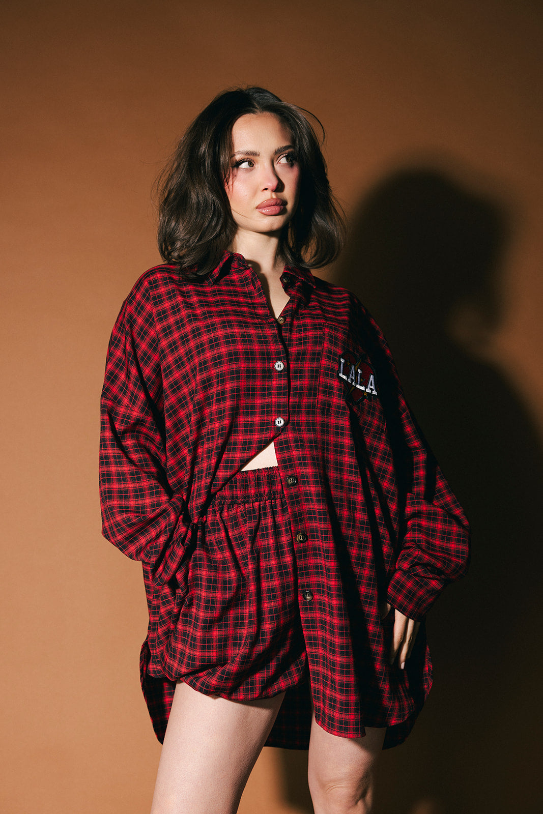 Woman wearing a red plaid outfit with a brand logo on a brown background