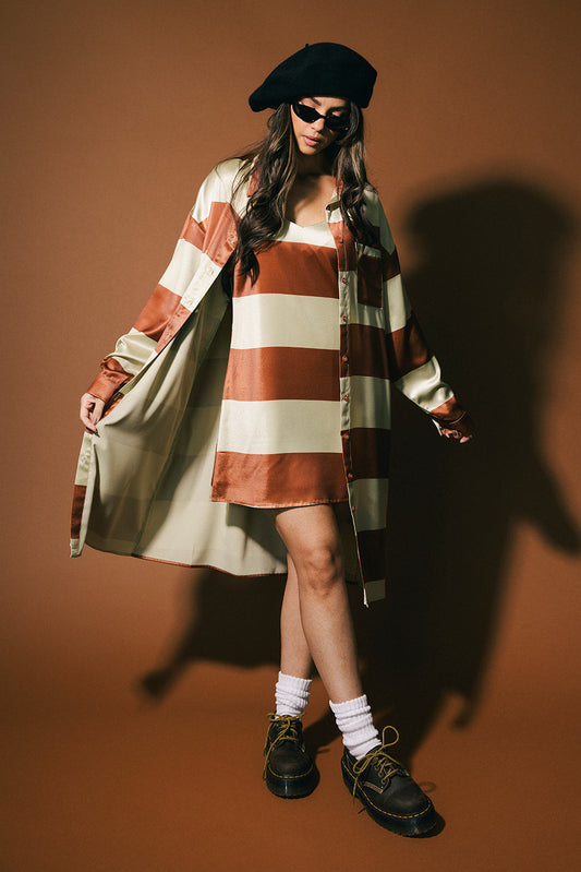 Person wearing a striped dress, matching duster, and beret against a brown background