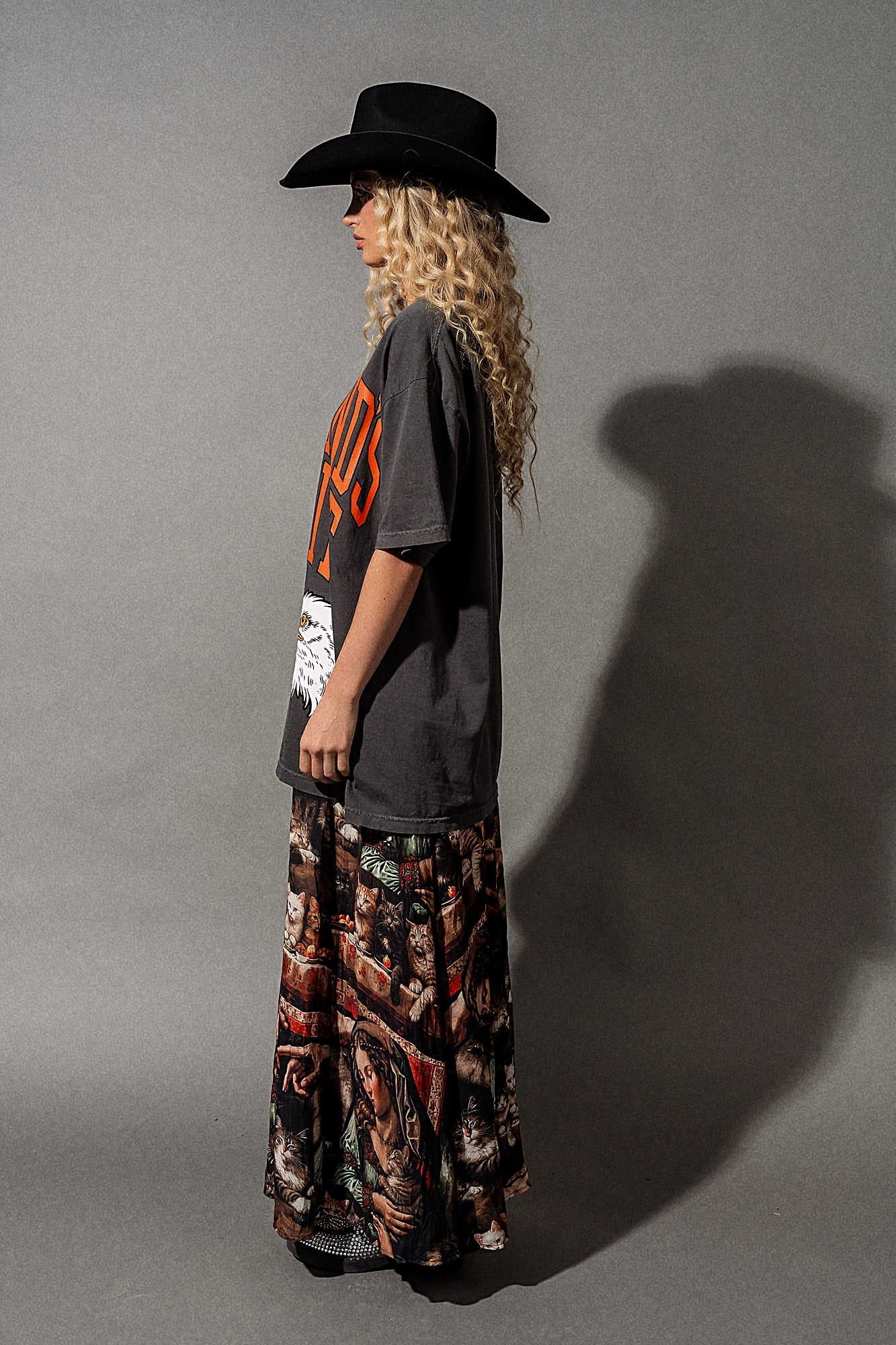 Person wearing a black hat, gray t-shirt with orange text, and patterned pants against a gray background