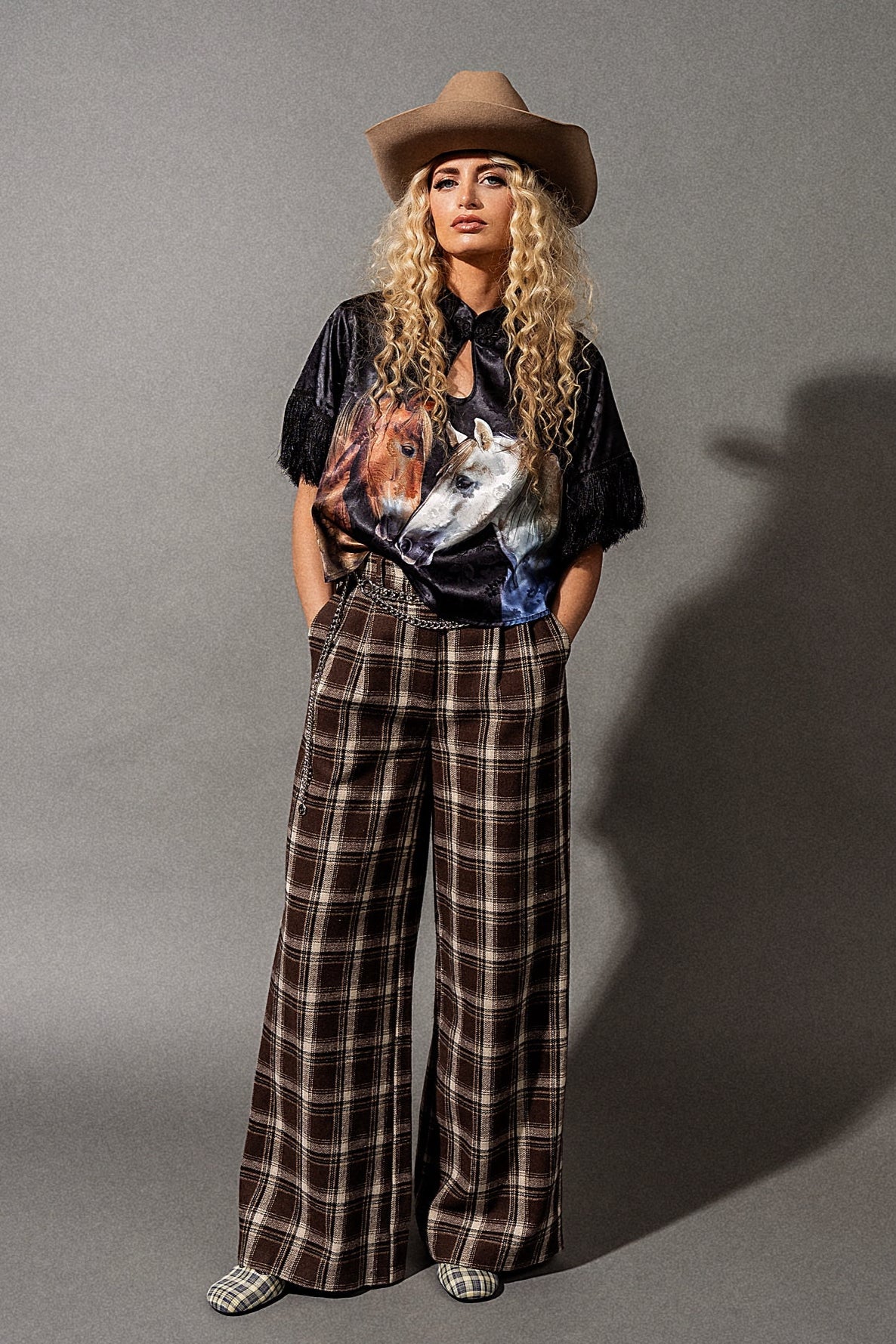 Person wearing a cowboy hat, graphic t-shirt, and plaid pants on a gray background