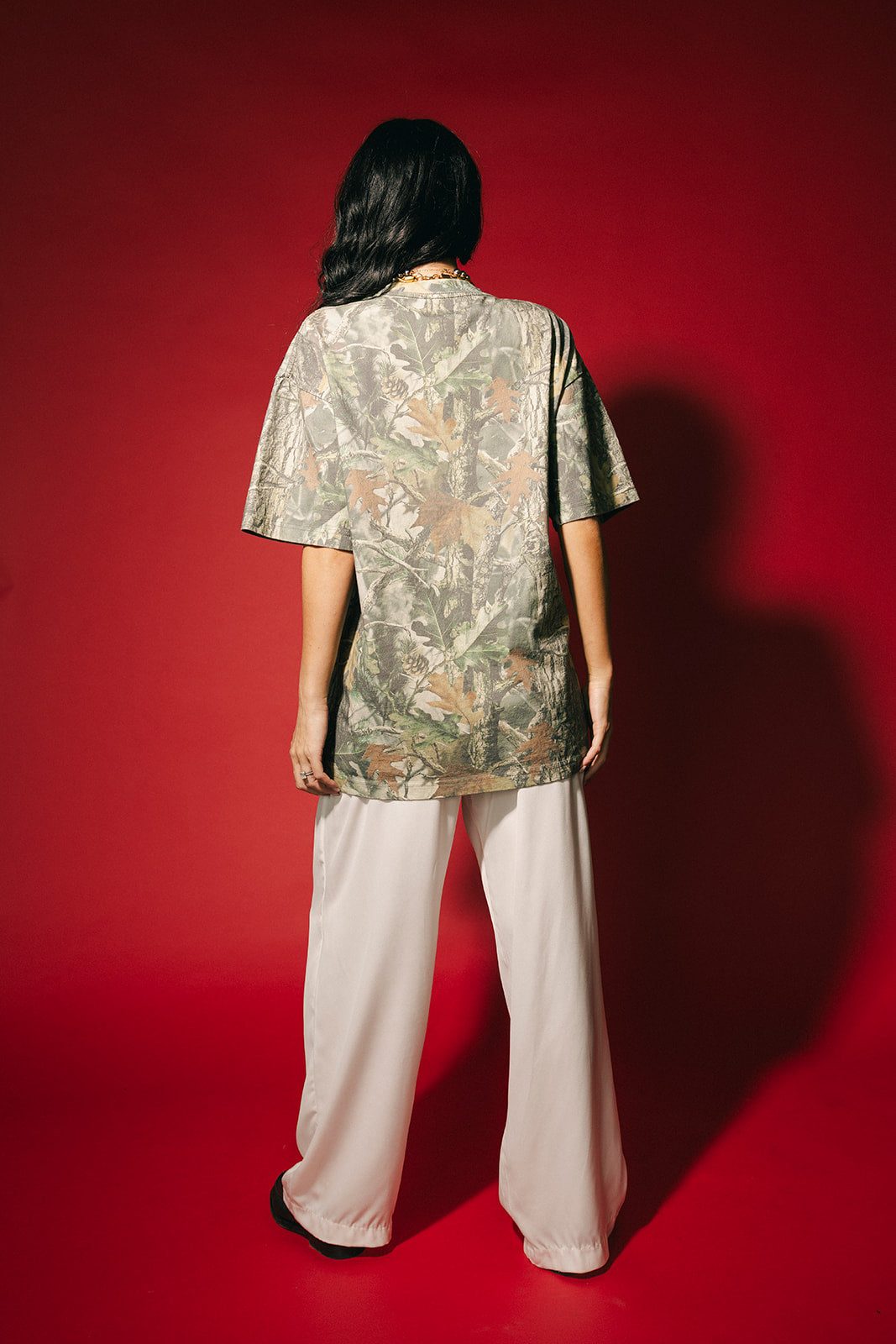 Person wearing a camouflage shirt and light-colored pants on a red background
