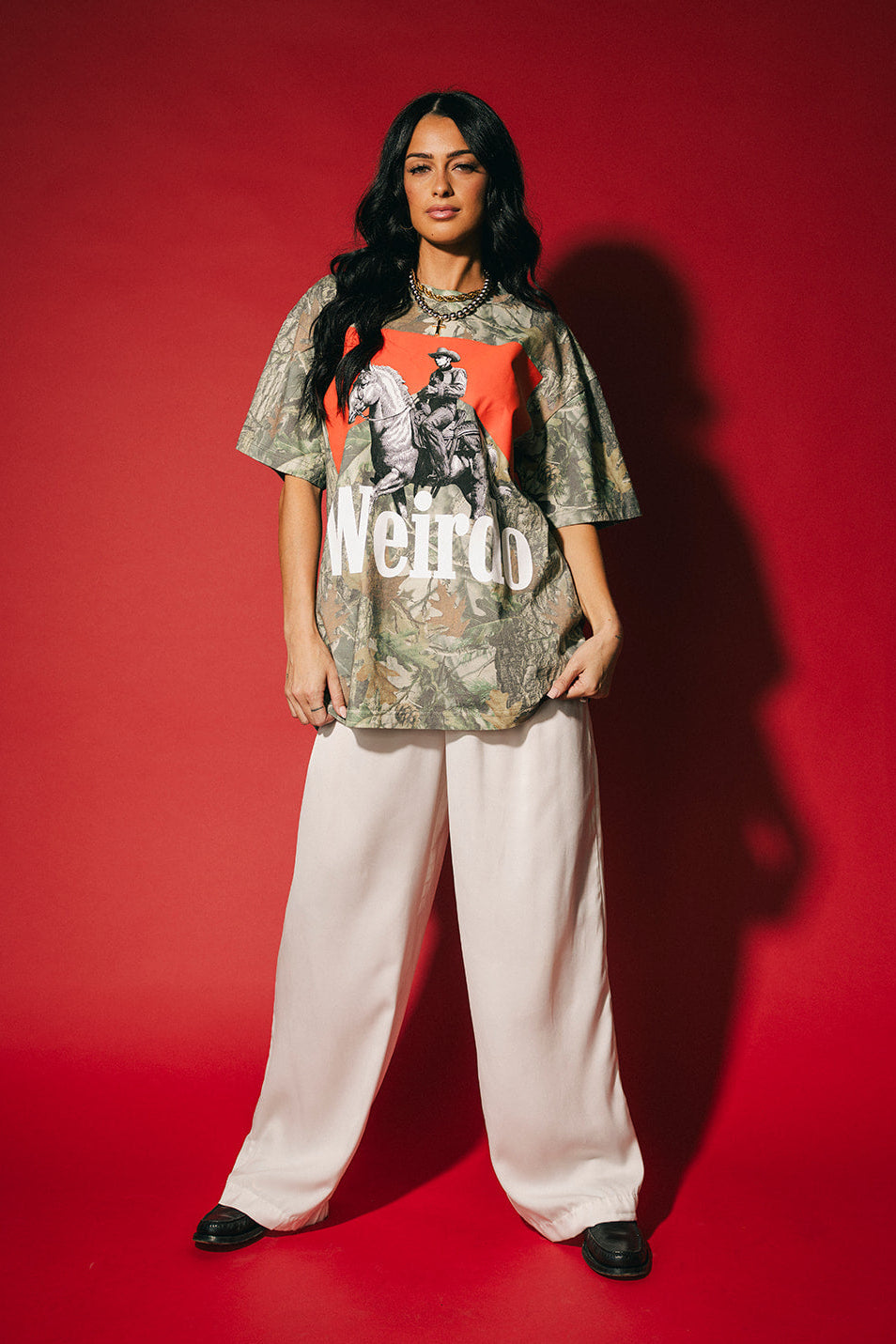 Person wearing a graphic t-shirt and white pants on a red background
