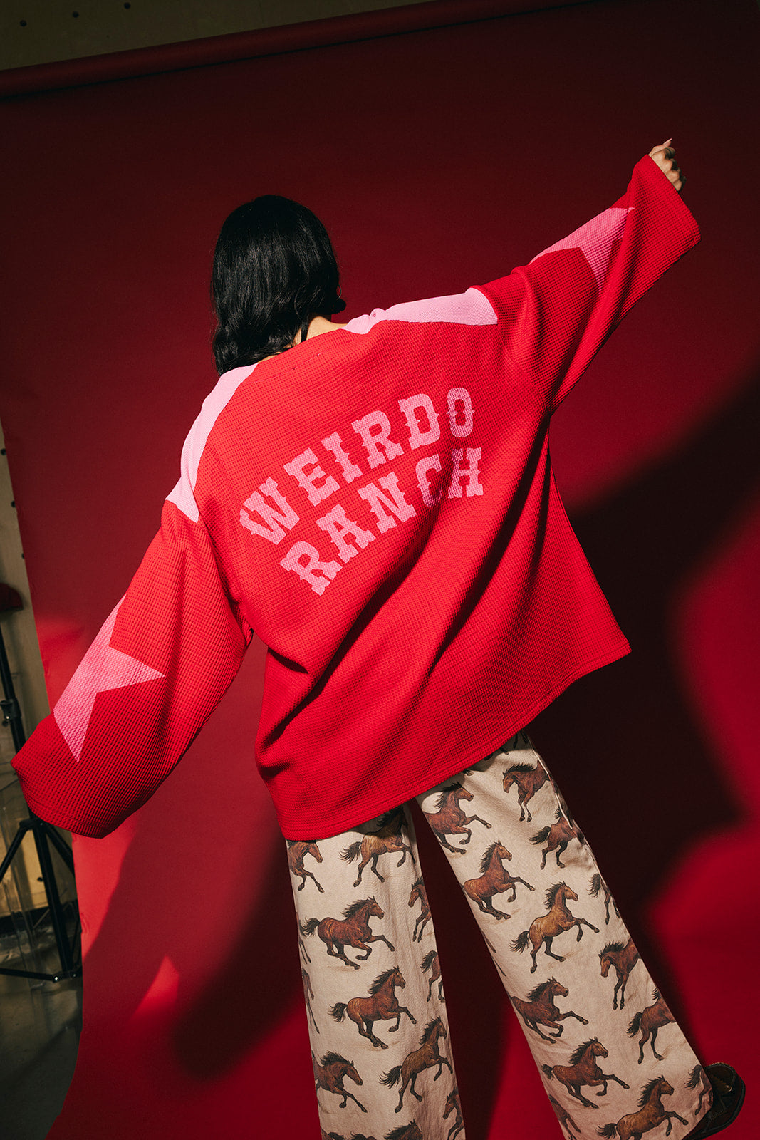 Person wearing a red and pink waffle knit hockey jersey inspired top with 'WEIRDO RANCH' text on the back against a red background