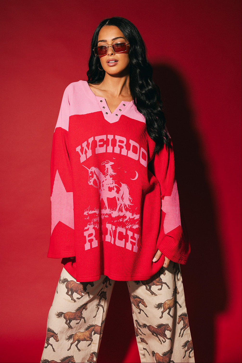 Person wearing a red and pink waffle knit hockey jersey inspired top with 'Weirdo Ranch' text and cowgirl riding a unicorn graphics on a red background