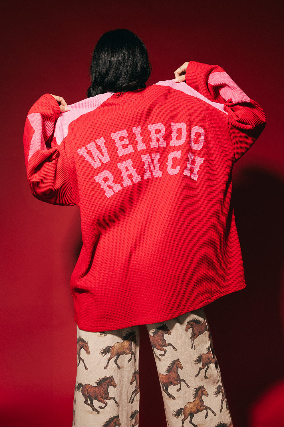 Person wearing a red and pink waffle knit hockey jersey inspired top with 'WEIRDO RANCH' text on a red background