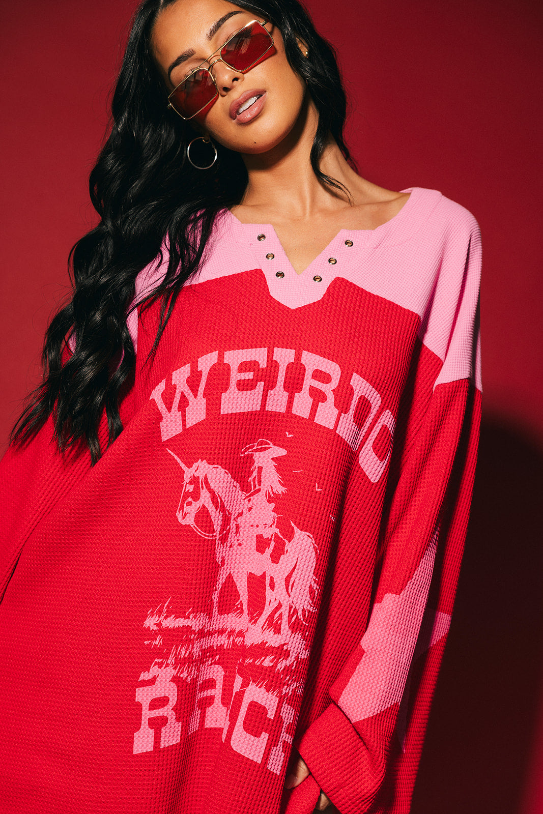 Person wearing a red and pink waffle knit hockey jersey inspired top with 'Weirdo Ranch' text and cowgirl riding a unicorn graphic on a red background