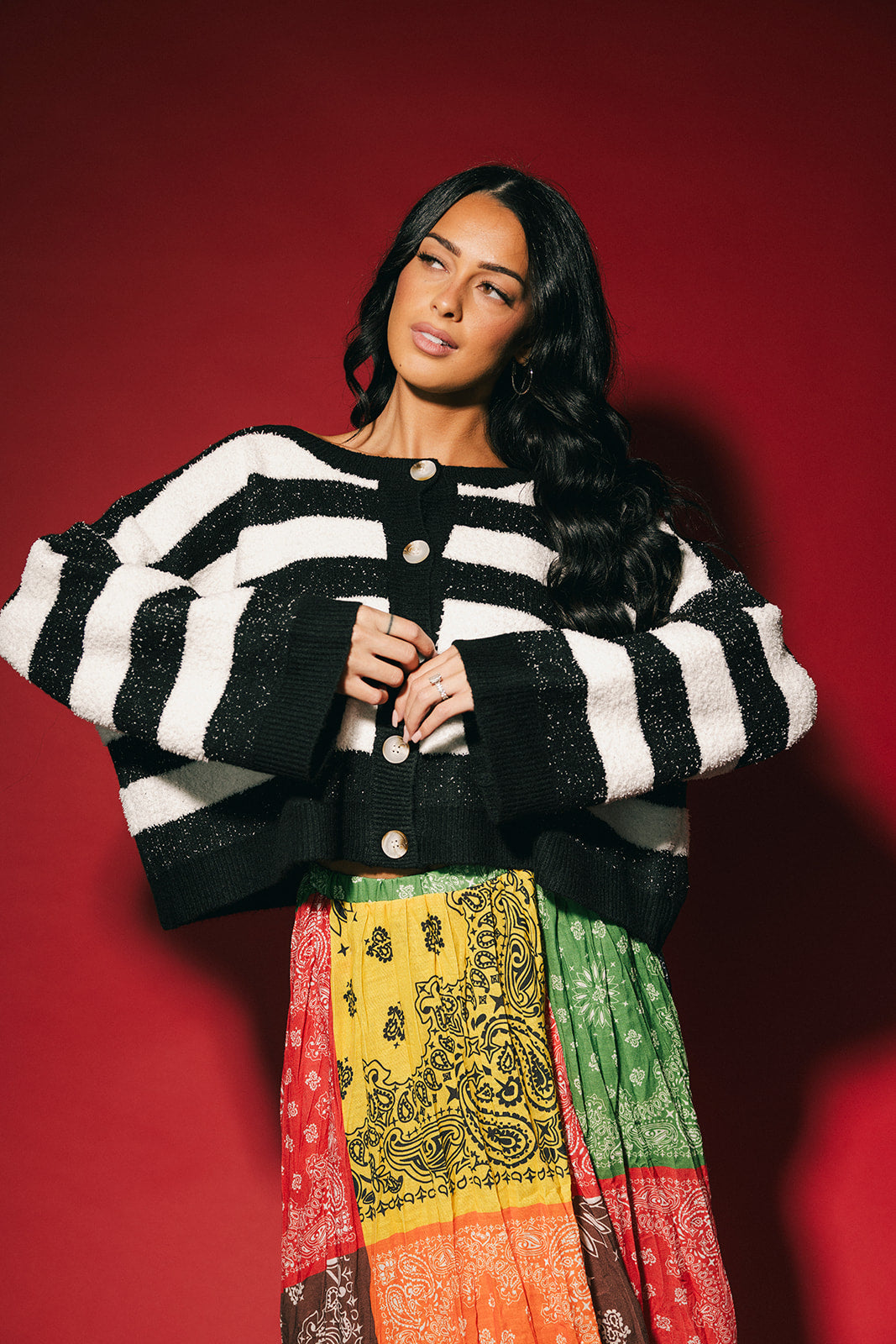 Woman wearing a black and white striped boxy cardigan with a colorful skirt against a red background