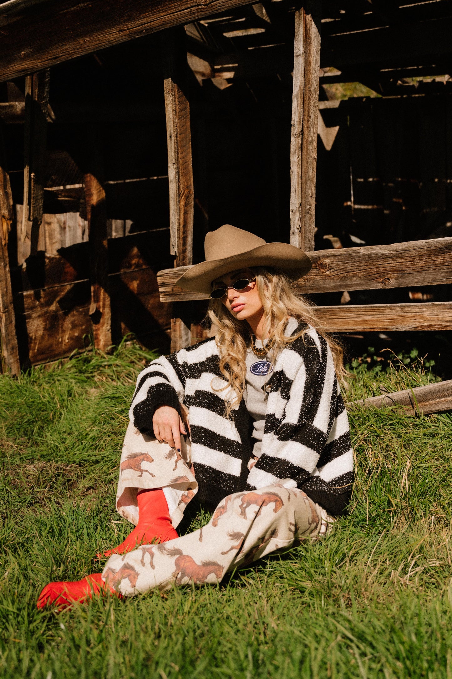 Person sitting on grass wearing a black and white striped boxy cardigan and cowboy hat.