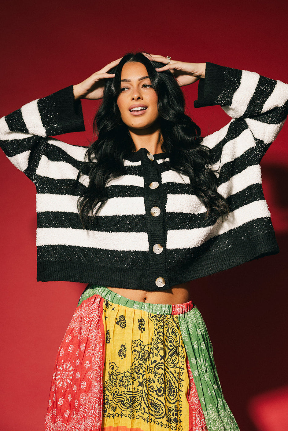 Woman wearing a black and white striped boxy cardigan with colorful skirt against a red background