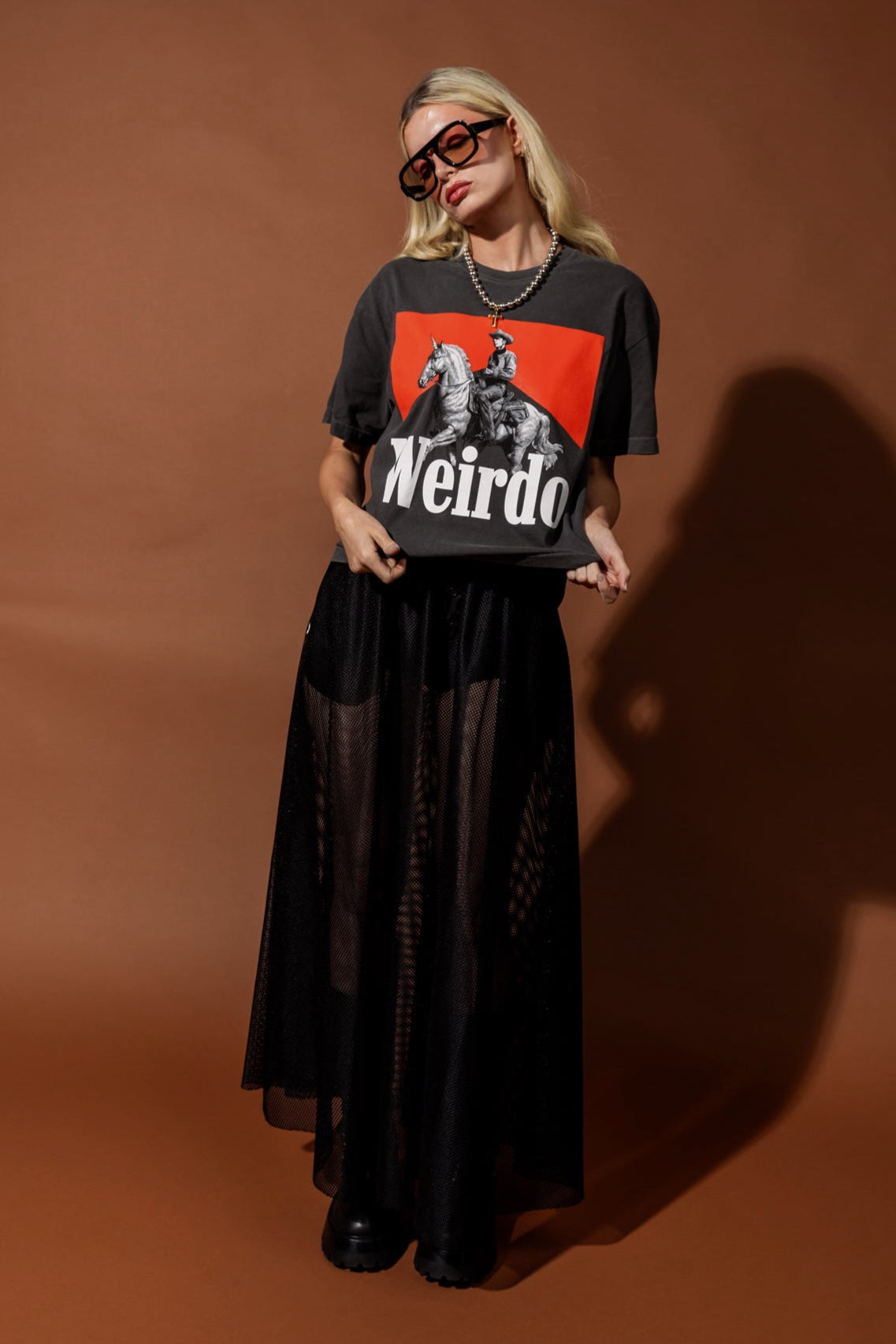 Person wearing a black t-shirt with a graphic design and text, standing against a brown background