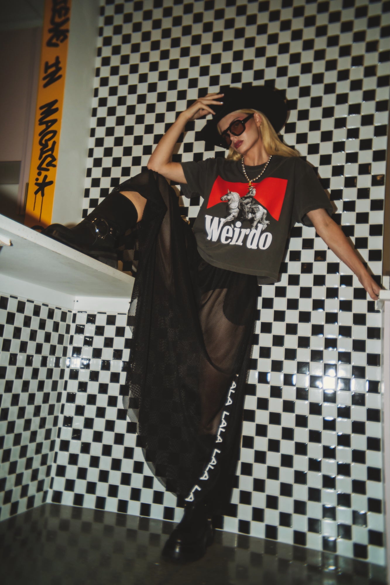 Person wearing a 'Weirdo' t-shirt in a room with black and white checkered walls.