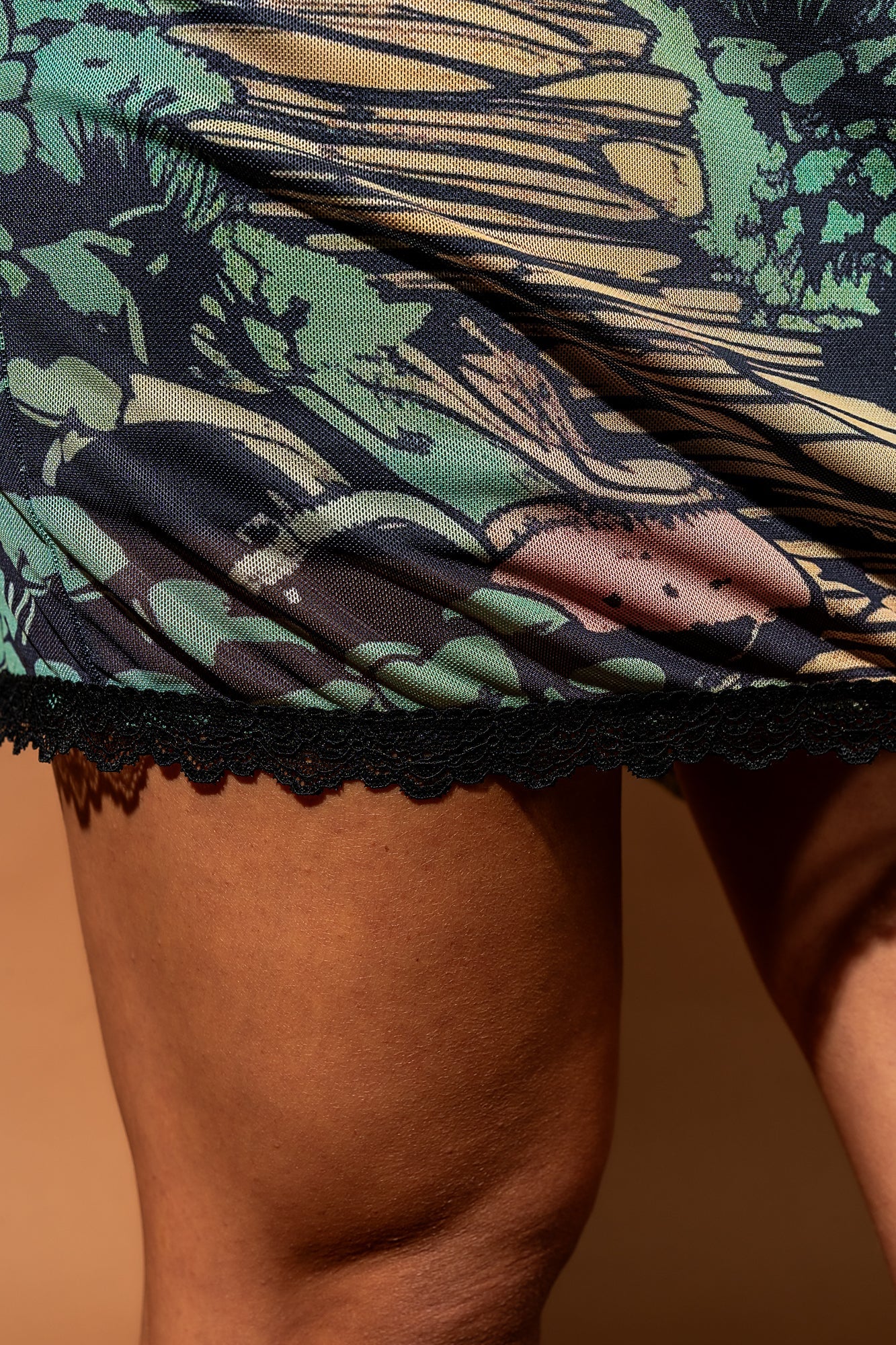 Close up photo of a girl wearing a mesh dress with a fairy print. Close up focuses on the black lace edge of the dress.