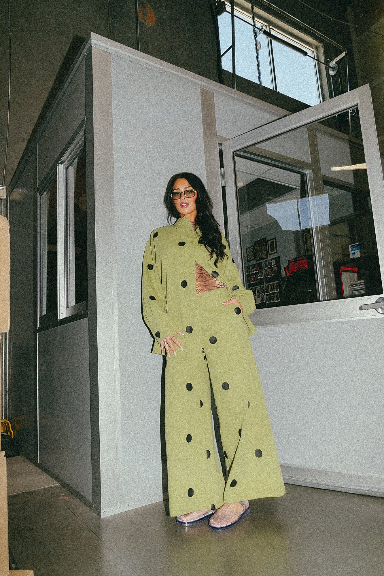 Girl/model standing against a door frame wearing a green shirt jacket with black polka dots and matching pants
