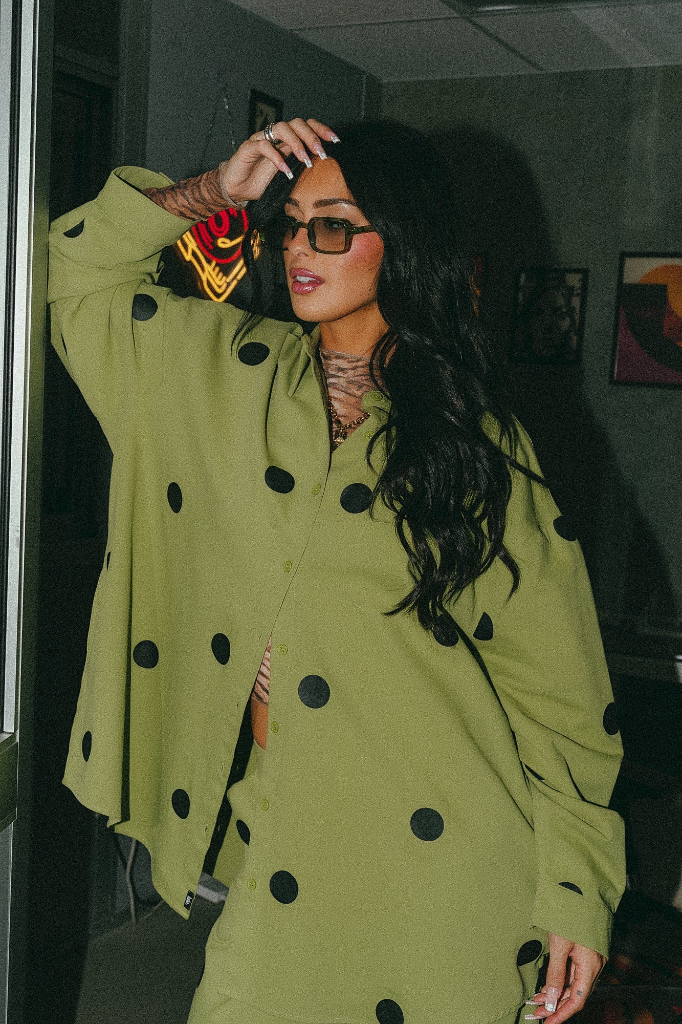Girl/model standing against a door frame wearing a green shirt jacket with black polka dots and matching pants