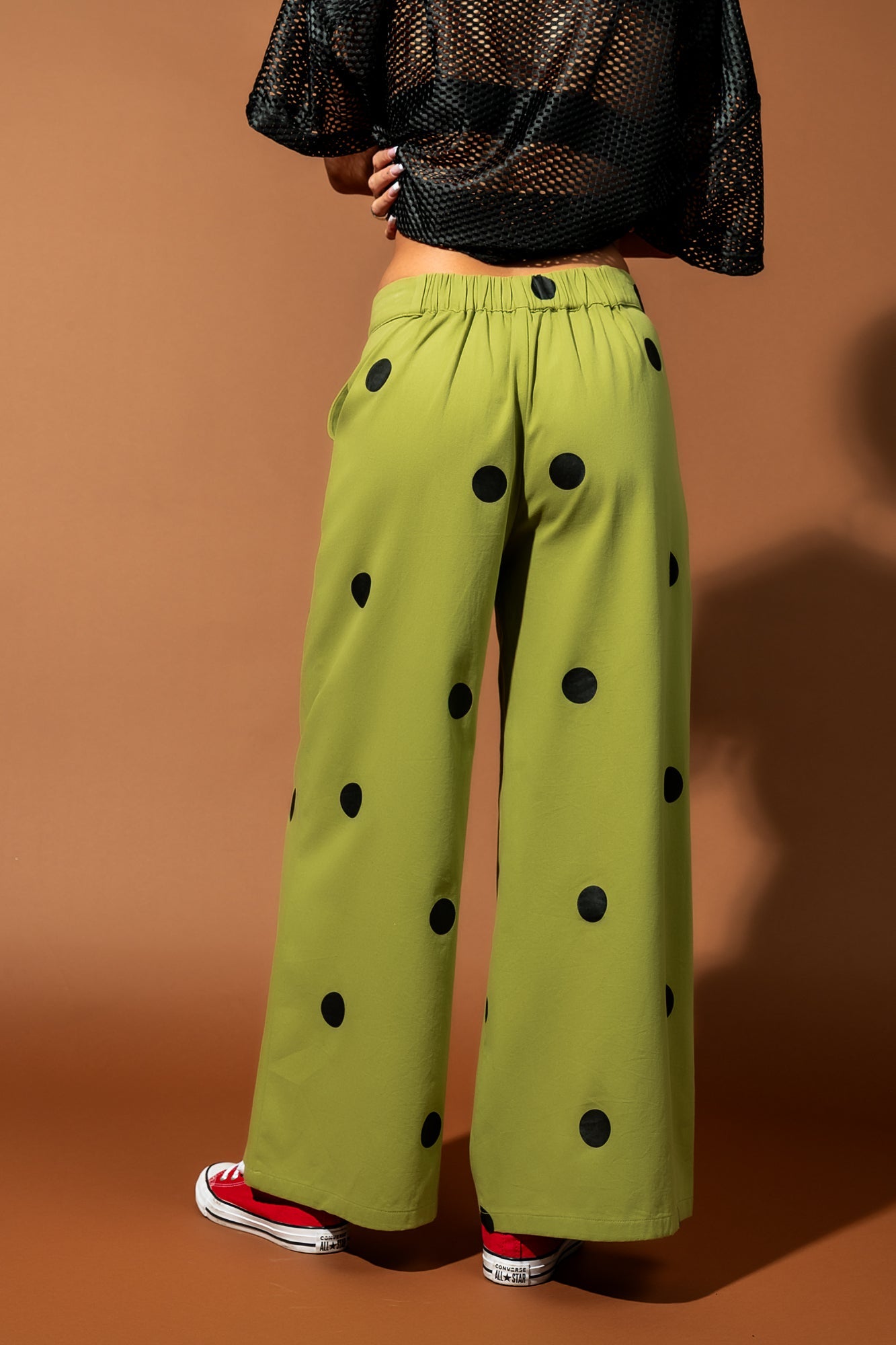 Close up photo of a model from the waist down wearing a pair of green pants with black polka dots