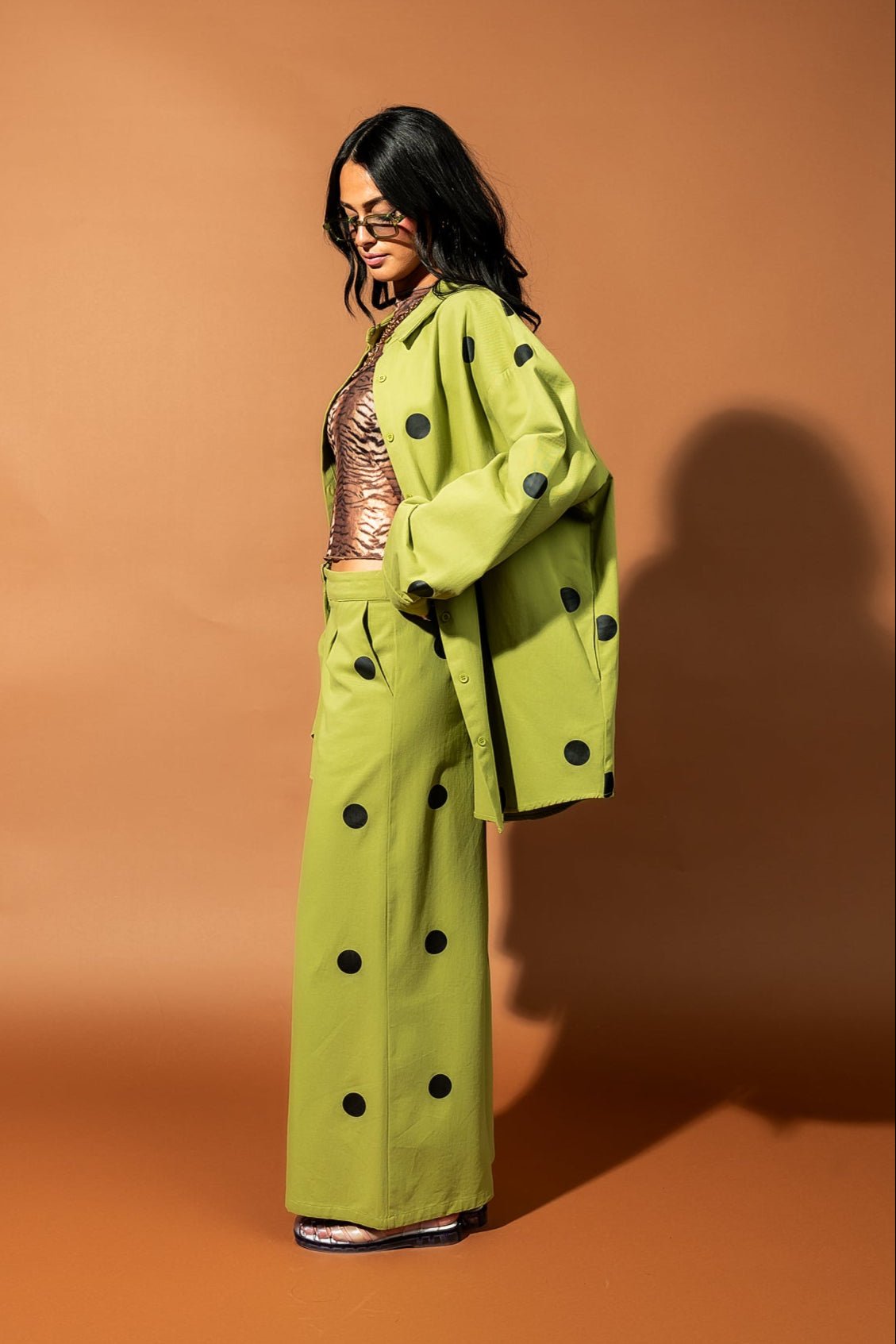 Girl/model standing against a brown backdrop wearing a green shirt jacket with black polka dots and matching pants
