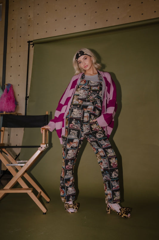 Model wearing Grandma's Couch Jacquard Overalls in Cute as a Kitten with a Love You Oversized Cardigan in Neverland Stripes next to a director's chair.