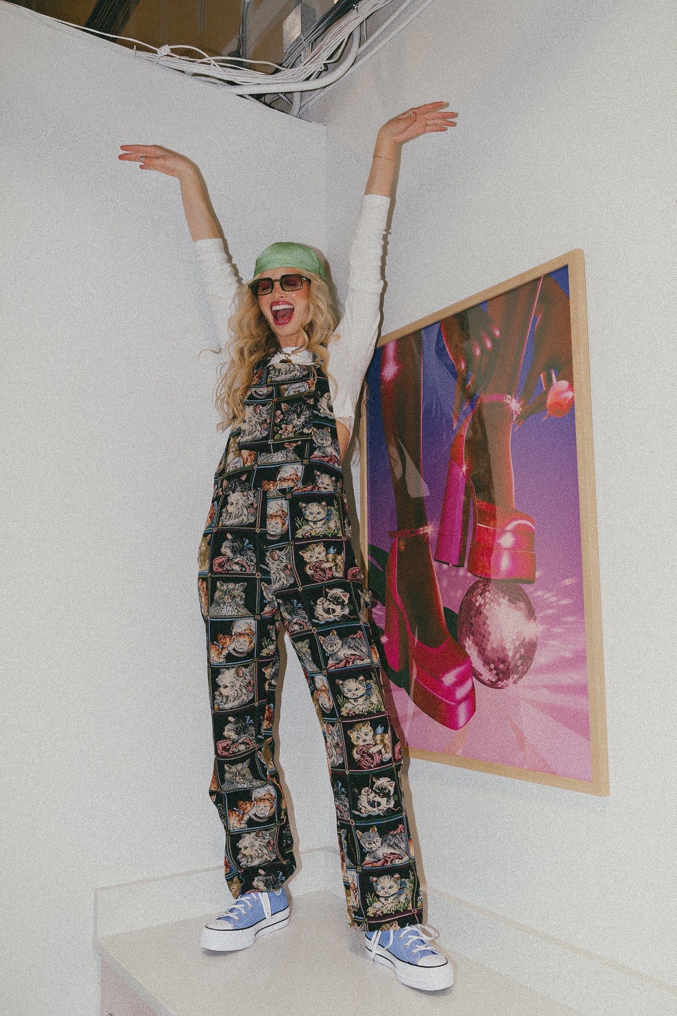 Model Meg is wearing the Grandma's Couch Jacquard Overalls in "Cute as a Kitten" pattern with a green headscarf and light blue high tops.