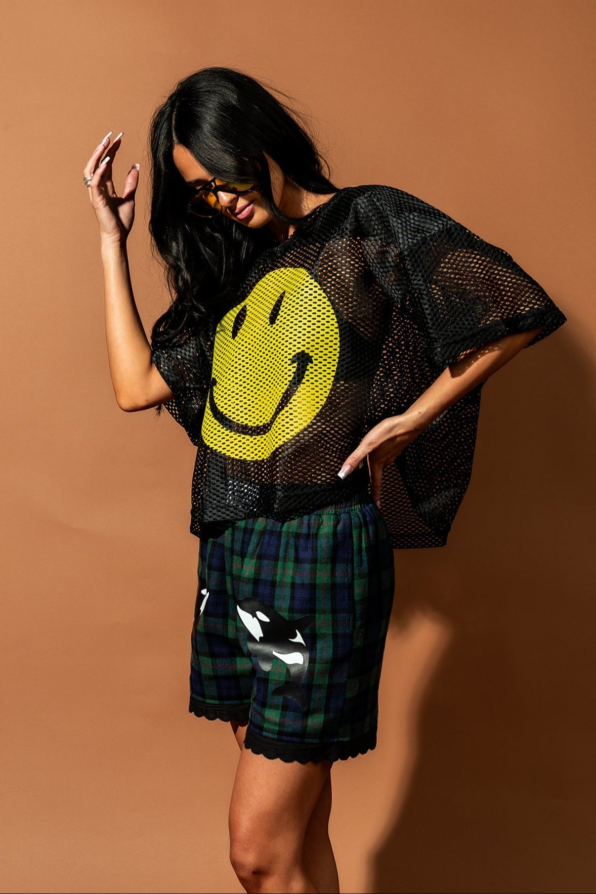 Girl/model wearing a black football jersey with a big yellow smile face printed on it with blue and green plaid shorts