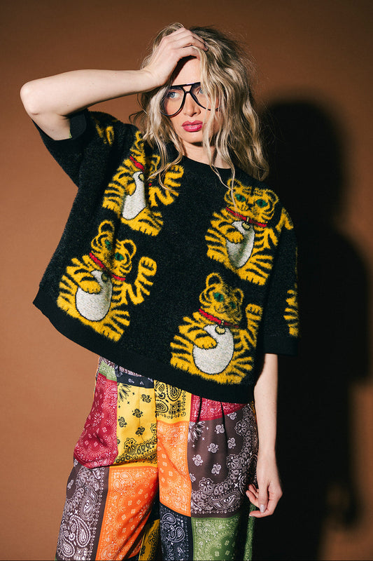 Person wearing a black sweater with tiger designs against a brown background