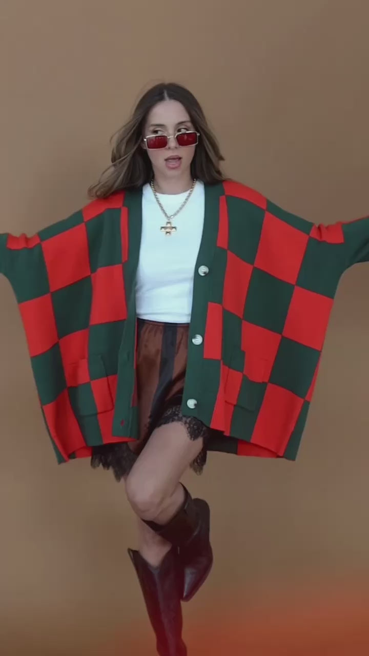 Video of a girl/model standing against a backdrop wearing a red and green checkered cardigan