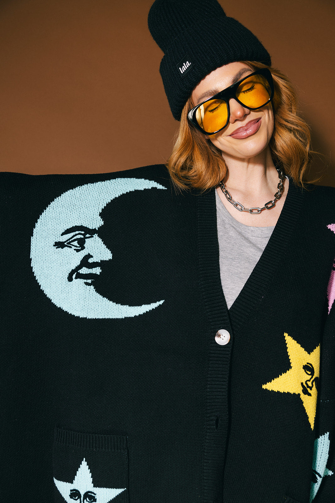 Person wearing a black cardigan with colorful stars and moons on a brown background