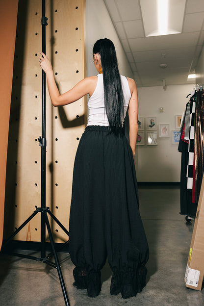 Person wearing a white top and black pants next to a backdrop.