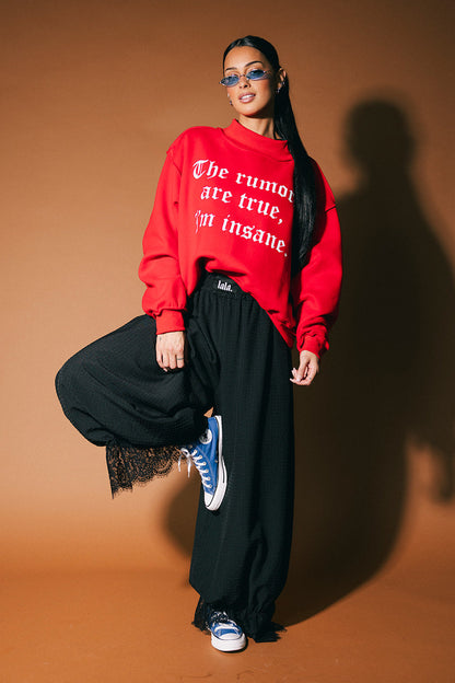 Person wearing a red sweatshirt with text, black pants, and blue sneakers on a brown background