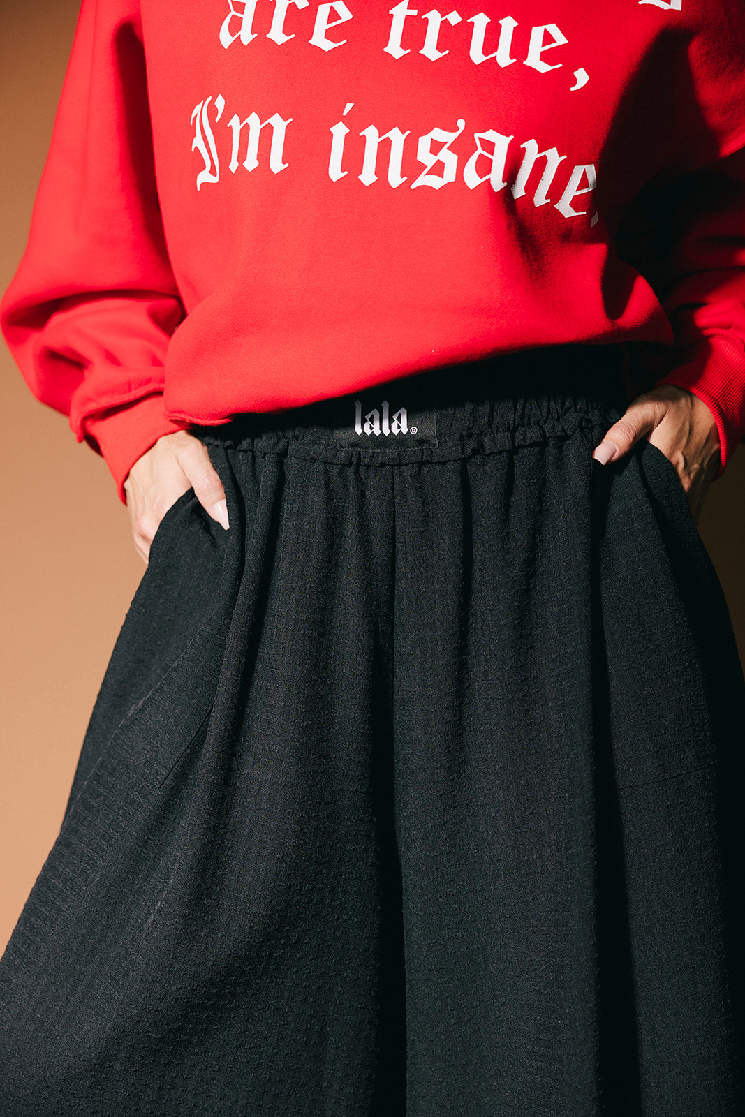 Person wearing a red sweatshirt with text and black pants against a brown background