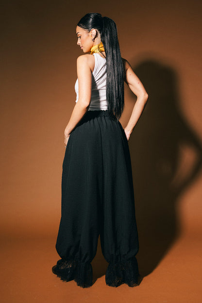 Woman wearing a white top and black bloomer pants against a brown background