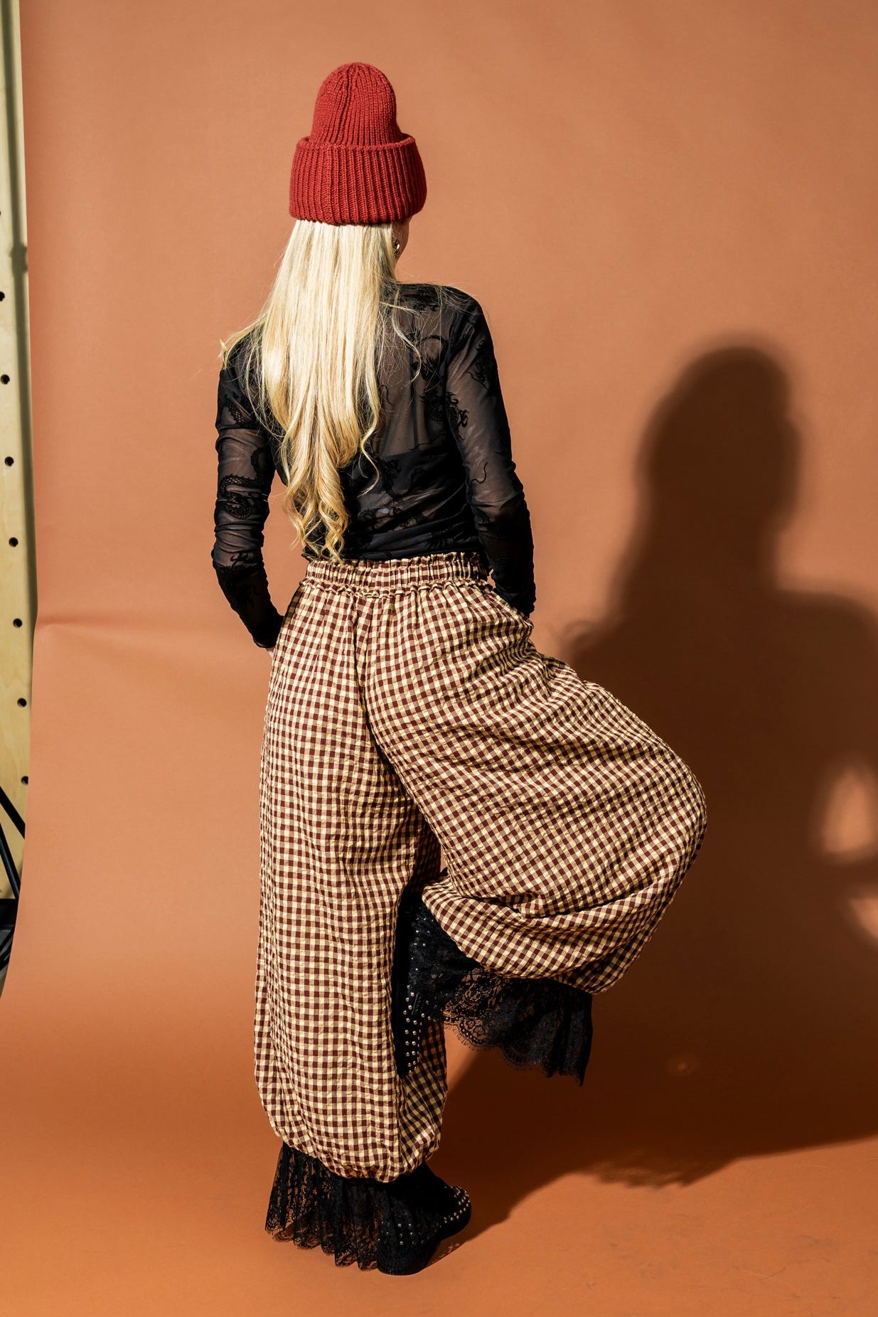 Person wearing a red beanie and checkered pants against a brown background