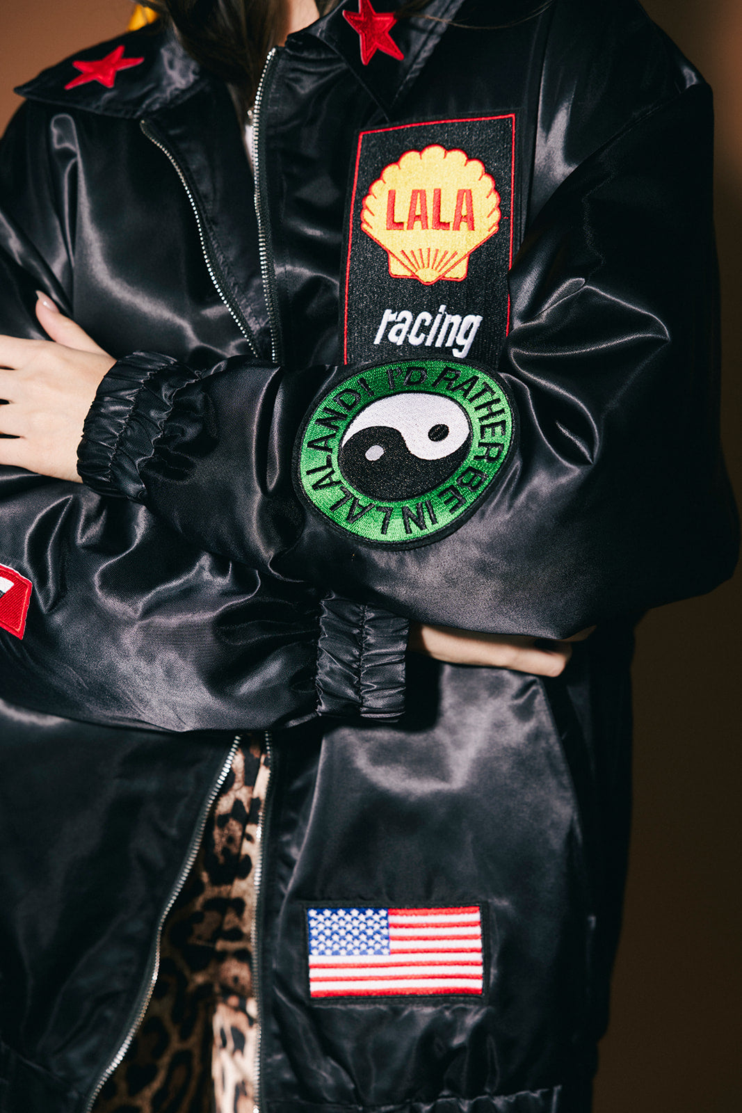 Black jacket with various patches including a logo, American flag, and others on a dark background.