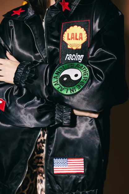 Black jacket with various patches including a logo, American flag, and others on a dark background.