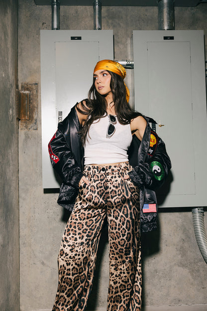 Person wearing a black leather jacket, white top, and leopard print pants in an industrial setting.