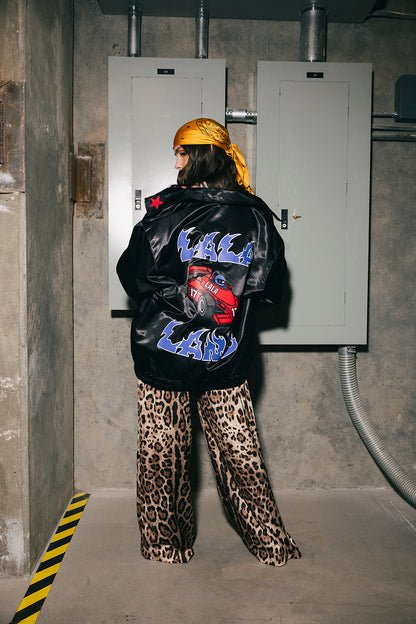 Person wearing a black jacket with colorful text and leopard print pants in an industrial setting