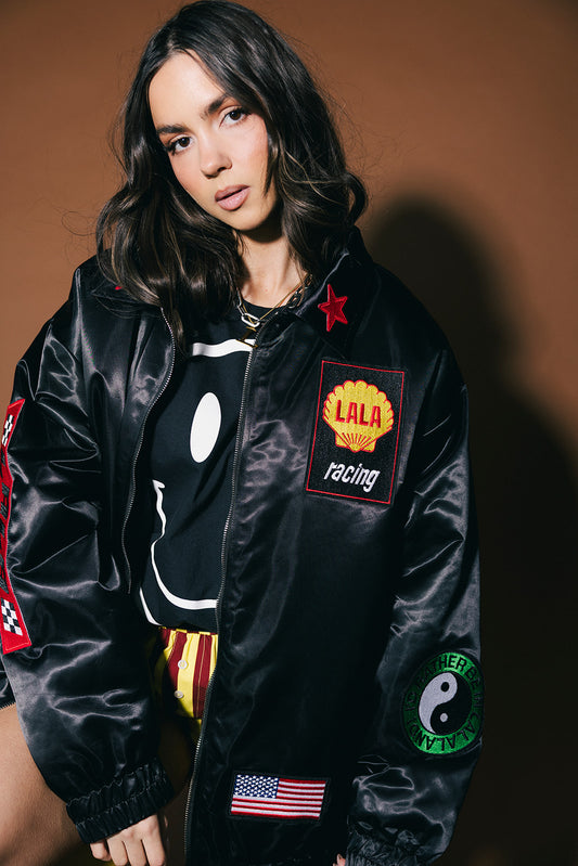 Person wearing a black jacket with various patches on a brown background