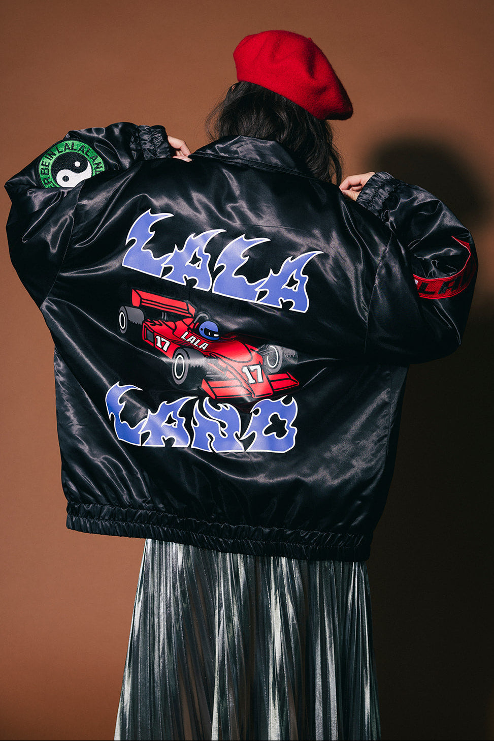 Person wearing a black jacket with colorful graphics and text on a brown background