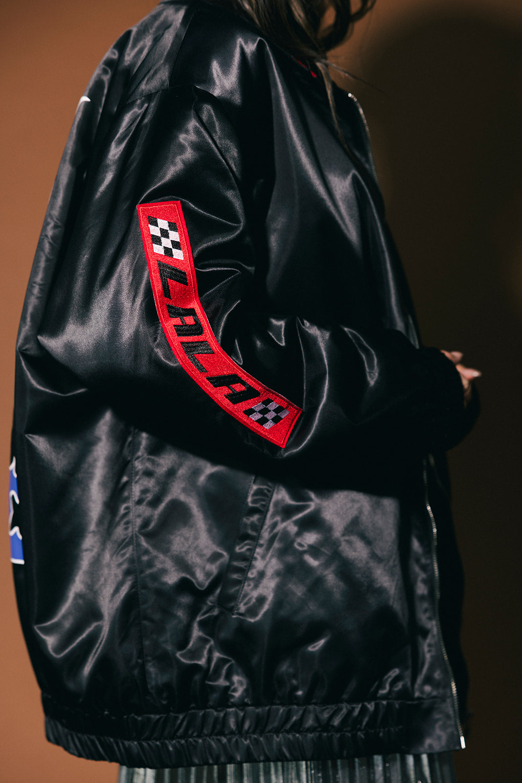Black satin jacket with red and white checkered logo on a dark background