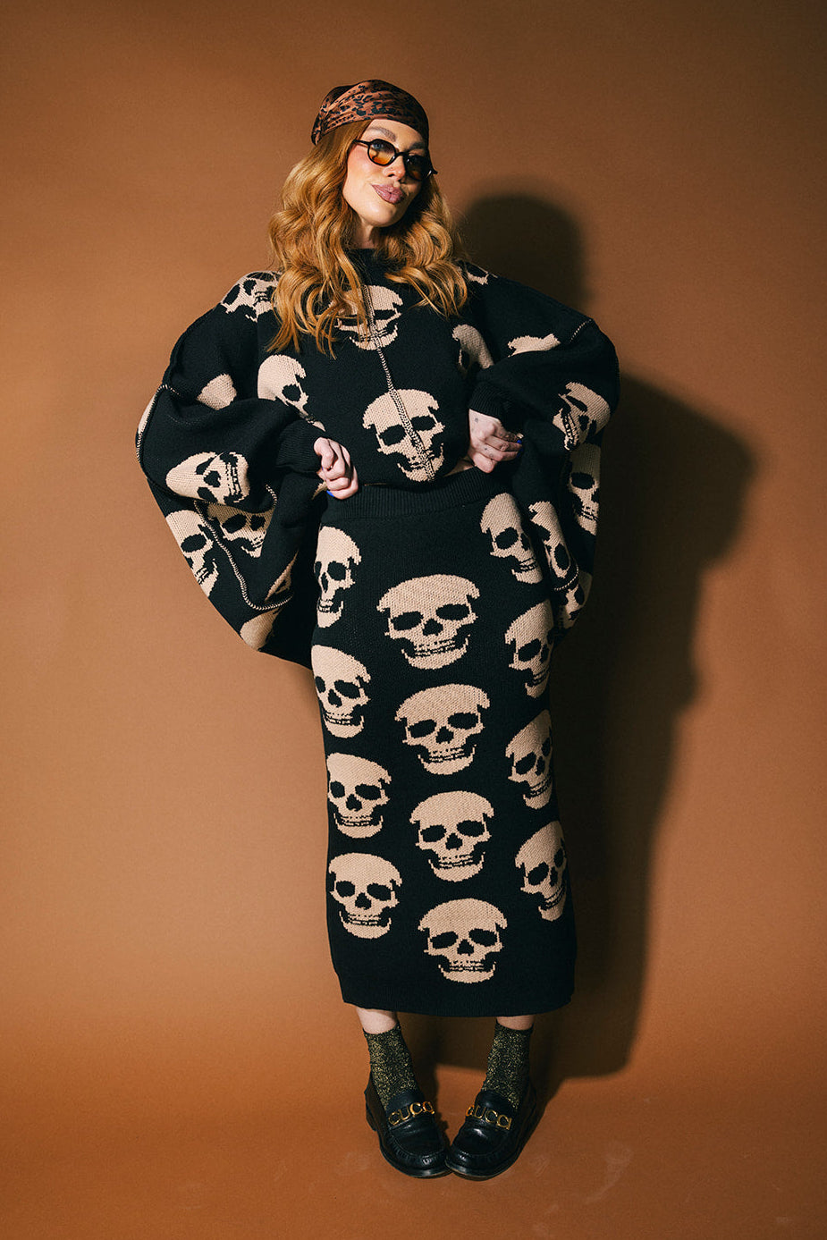 Person wearing a black knit skirt with skull pattern against a brown background