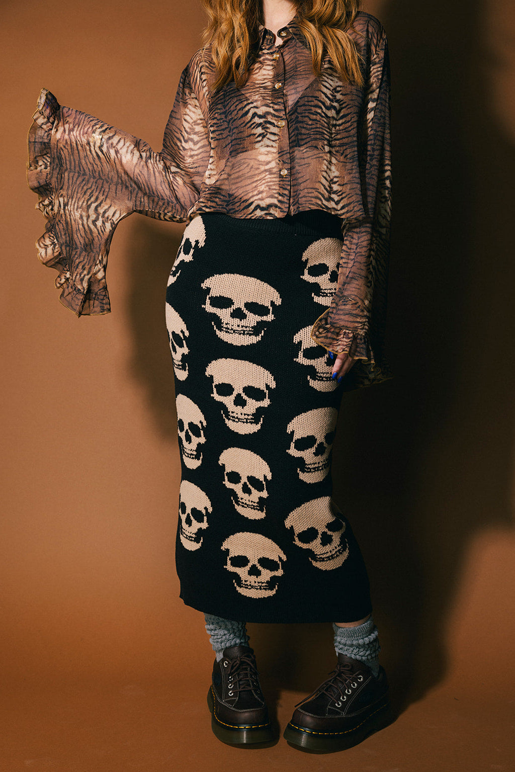 Person wearing a black knit skirt with skull pattern against a brown background