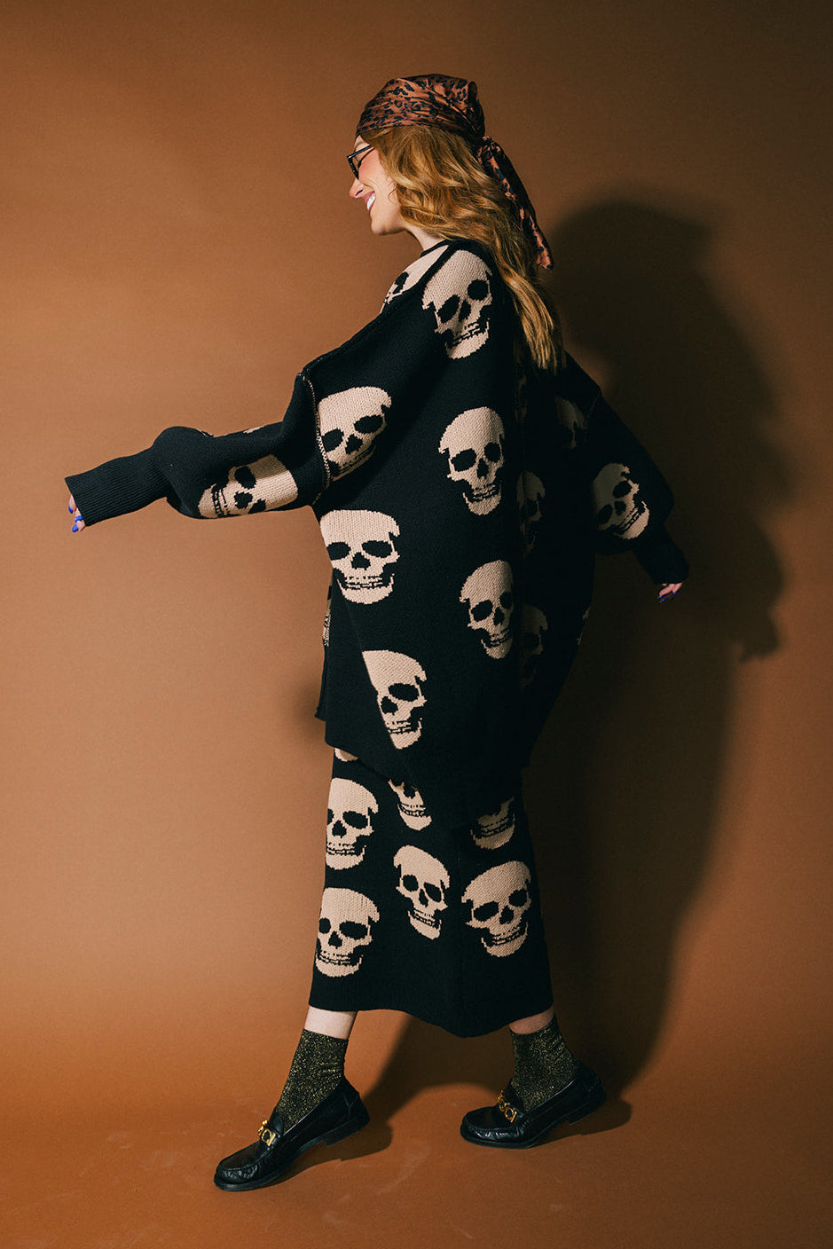 Person wearing a black knit skirt with skull pattern against a brown background