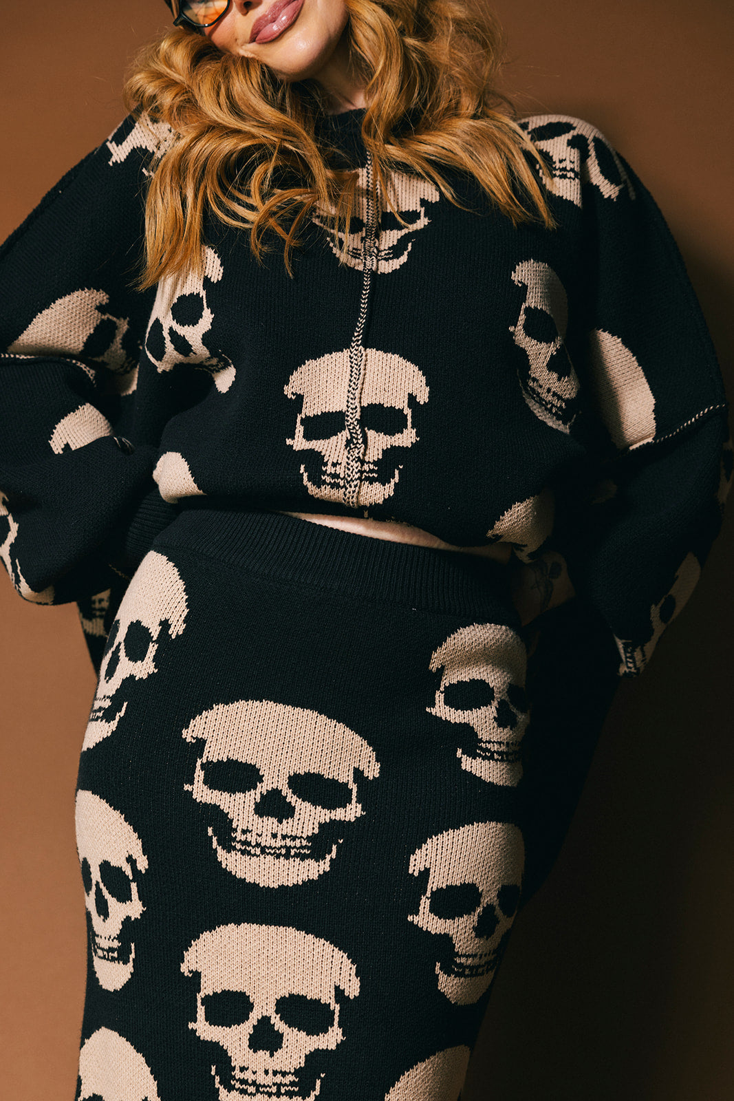 Person wearing a black knit skirt with skull pattern against a brown background