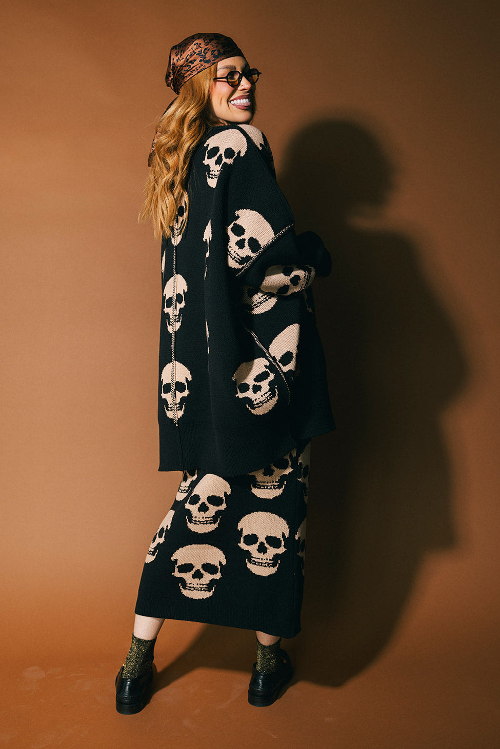 Person wearing a black skull-patterned sweater with a brown background