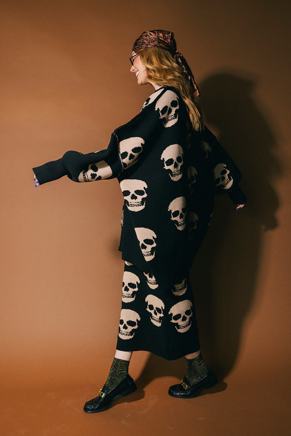 Person wearing a black skull-patterned sweater with a brown background