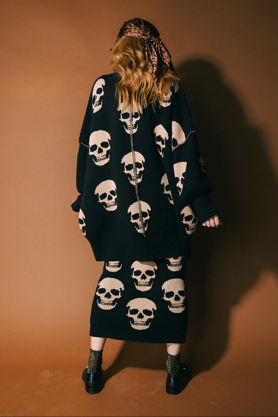 Person wearing a black skull-patterned sweater with a brown background