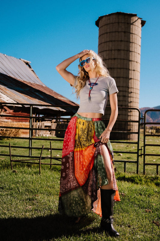 Woman in a patchwork style banana print pleated midi skirt with a side slit standing in front of a barn and silo